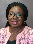 Woman with glasses, wearing a pink floral-patterned jacket over a black top, smiles against a plain background.