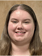A woman with long brown hair smiles at the camera against a plain beige background.