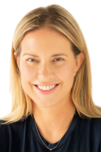 A woman with straight blonde hair and light skin smiles at the camera, wearing a dark shirt and a thin necklace, against a plain light background.