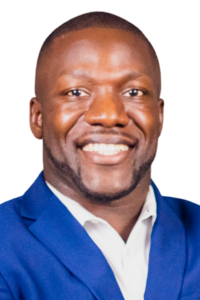 A man wearing a blue suit jacket and white shirt smiles at the camera against a plain white background.
