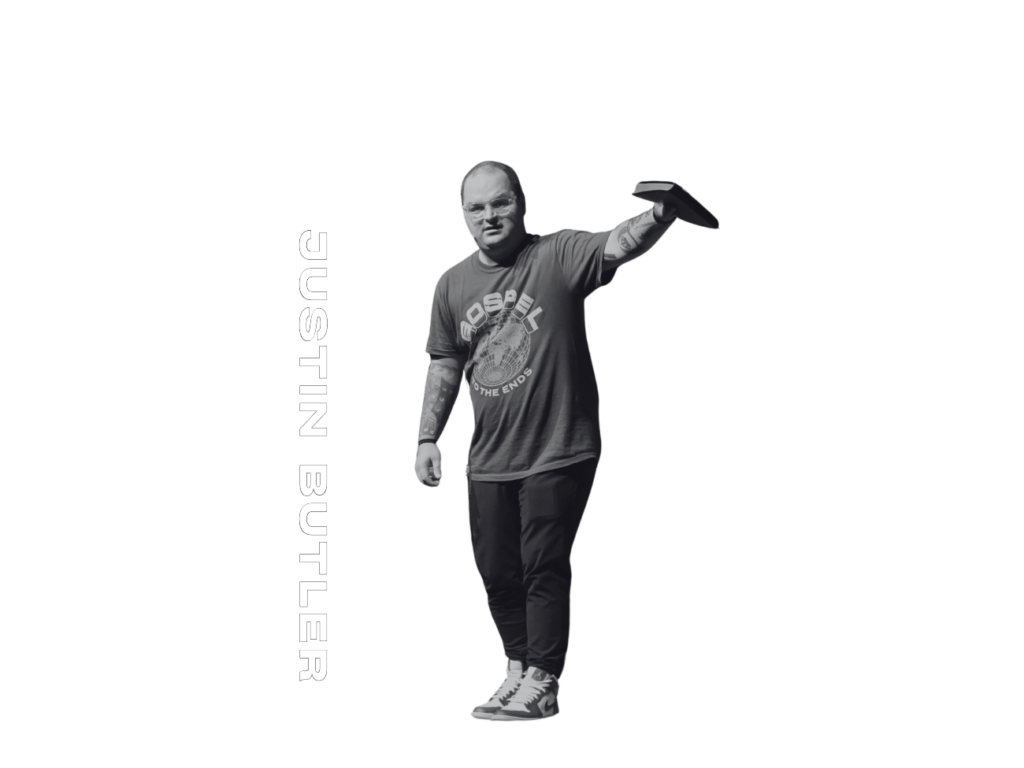 A man in casual clothing holds a disc in one hand. Text reads “SPEAKER” and “JUSTIN BUTLER.” The background is plain.