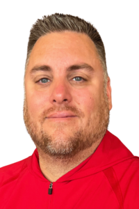 A man with short, grayish hair and a trimmed beard, wearing a red jacket, poses against a plain white background.